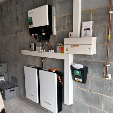 Solar inverter and battery storage system mounted on a grey wall.