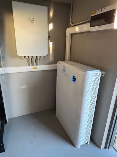 A white electrical cabinet with cables, mounted in a grey utility room.